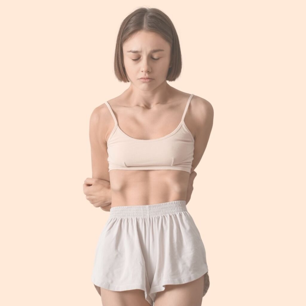 Fille aux cheveux mi-longs en short et crop-top montrant ses bras maigres et ses côtes