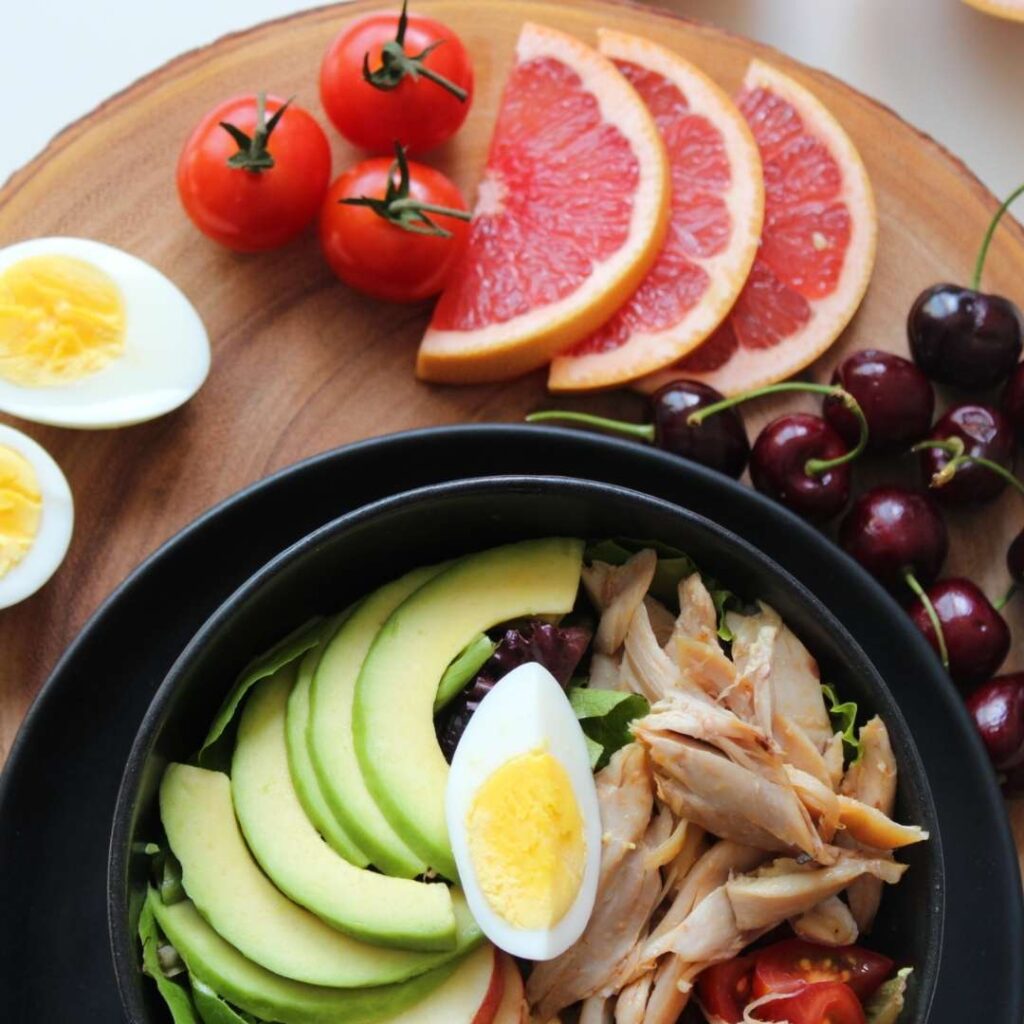 Aliments sains : deux moitiés d'oeufs durs, 3 tomates cerises, 3 tranches de pamplemousse rose, des cerises, une assiette de salade poulet, avocat, laitue