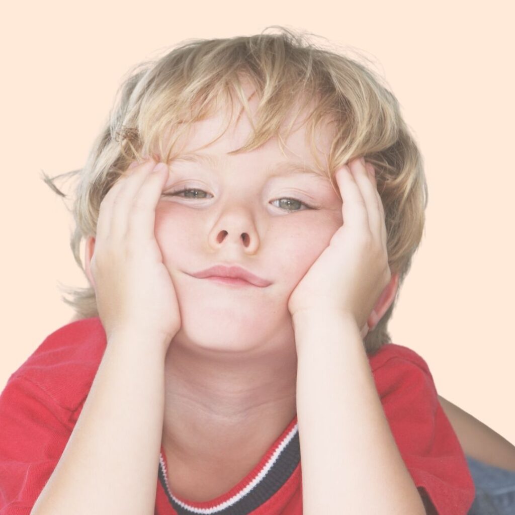 Petit garçon blond, portant un tee-shirt rouge, allongé, il se tient le visage entre ses deux mains